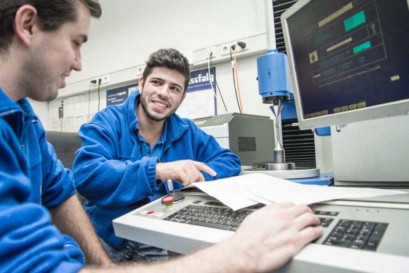 Zwei männliche Mitarbeiter besprechen gemeinsam ihre Arbeit an einer Maschine